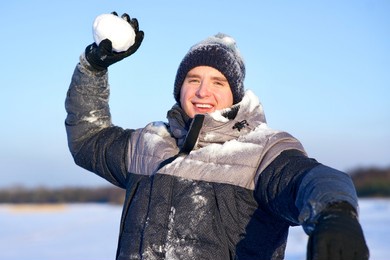 young handsome positive happy man is playing in snowball in a winter snowy forest, smiling, having fun with snow. guy is throwing a snowball.