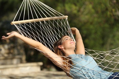 happy woman relaxing on a hammock on holidays and raising arms in the mountain