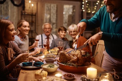 close up of father carving thanksgiving turkey during family meal at dining table.