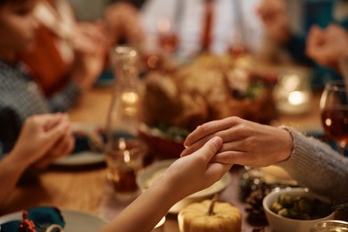 close up of extended family saying grace during thanksgiving dinner at dining table.