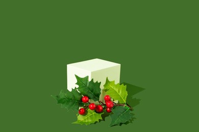 white gift box and holly berry branch on grren background. christmas present concept. copy space.