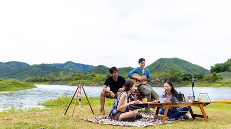 group of asian people enjoy and fun outdoor lifestyle hiking and camping together on summer travel vacation. man and woman friends having breakfast drinking brewed coffee near the tent in the morning.