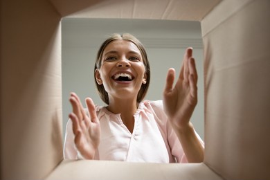 happy laughing young woman putting arms into box, feeling excited receiving order from internet store. joyful female customer satisfied with fast delivery service, getting parcel, shipping concept.