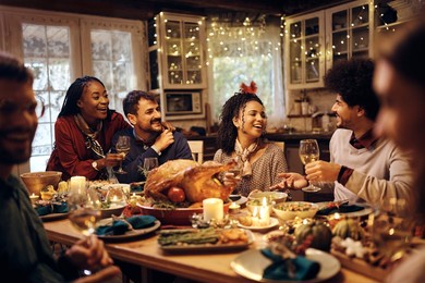 young happy friends talking while having lunch together on thanksgiving in dining room. focus is on african american woman.