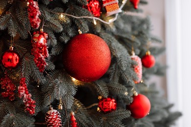 stylish christmas decorations on the tree, beautiful toys, balls, cones and lights in red colours. christmas cozy atmosphere in living room, new year. festive interior design