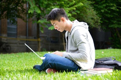 male college student use laptop on a grass at a campus 