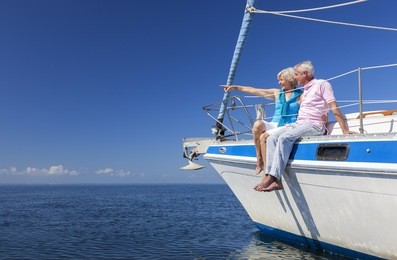 a happy senior couple sitting on the side of a sail boat on a calm blue sea looking and pointing to a clear horizon