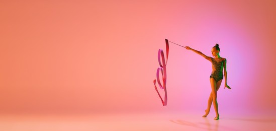 studio shot of young charming girl, rhythmic gymnast training with sports equipment isolated over pink background in neon light filter. dance, music, emotions, challenges, motivation and ad