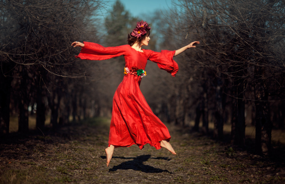in autumn park floating girl in a red dress with a wreath on his head like a fairy tale.