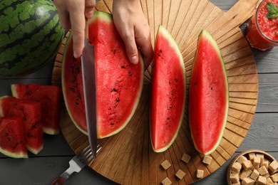 woman cutting delicious watermelon at grey wooden table, top view