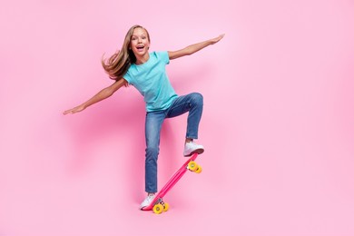 full length photo of sweet excited small kid wear turquoise t-shirt riding skateboard empty space isolated pink color background