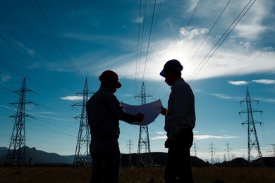 silhouette of two engineers standing at electricity station, discussing plan