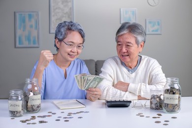 savings concept. asian old elderly senior couple grandparents husband and wife saving money, economizing pension, putting coin into money box, thinking over pension plan