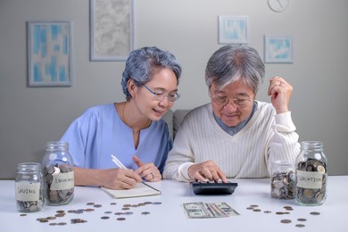 savings concept. asian old elderly senior couple grandparents husband and wife saving money, economizing 
pension, putting coin into money box, thinking over pension plan