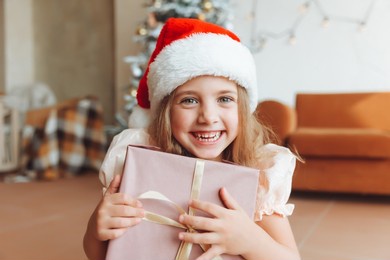 a little girl in a white dress is sitting on the floor and holding a new year's gift against the background of a christmas tree. the concept of christmas and new year.
