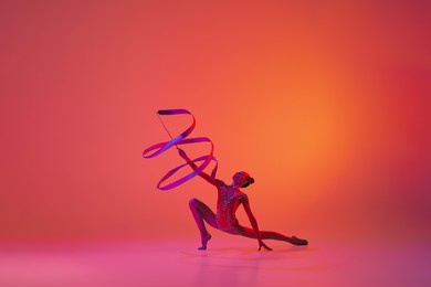 exercise with ribbon. young flexible teen girl rhythmic gymnast in motion, action isolated over pink background in neon light. sport, beauty, competition, flexibility, active lifestyle. performance