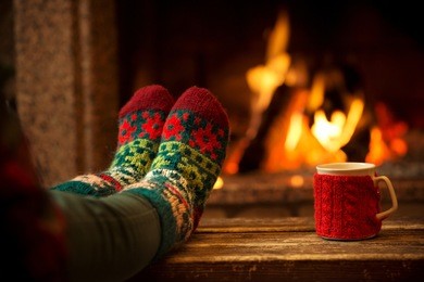feet in woollen socks by the christmas fireplace. woman relaxes by warm fire with a cup of hot drink and warming up her feet in woollen socks. close up on feet. winter and christmas holidays concept. 