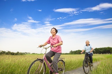happy asian elderly seniors couple biking in farm with blue sky background