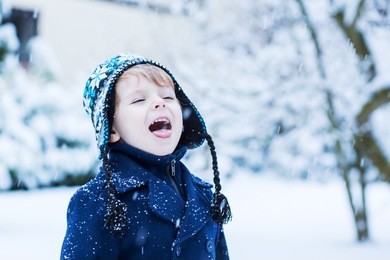 portrait of little toddler boy in winter clothes with falling snow