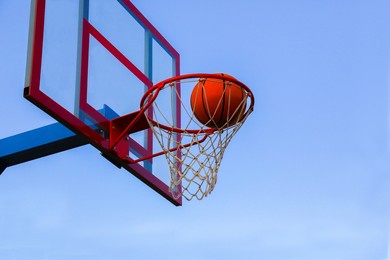  a basketball in a basket on an outdoor basketball court. a basketball is a goal in a basketball basket against the sky. 