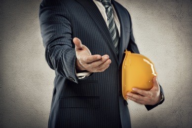 portrait of male architect with safety hardhat greeting his partner. young man builder showing handshake. partnership concept.  