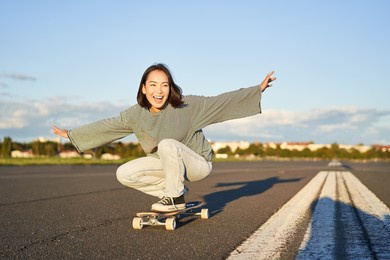 freedom and happiness. happy asian girl riding her longboard on an empty sunny road, laughing and smiling, skateboarding.