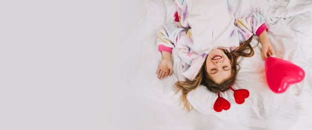 the child is holding a balloon in the shape of a heart. a little girl lies on the bed and holds a heart.valentine's day