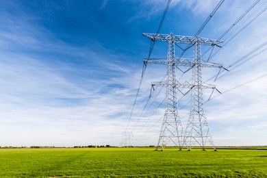 high voltage lines and power pylons in a flat and green agricultural landscape on a sunny day with cirrus clouds in the blue sky.