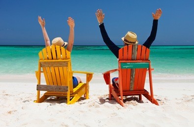 happy couple sitting on colorful chairs at tropical beach enjoying caribbean vacation