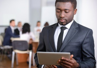 portrait of black businessman, people group in background at modern bright office indoors