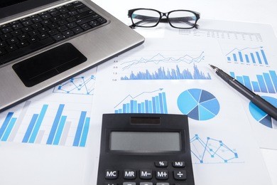 closeup of calculator on business chart with pen, laptop, and glasses