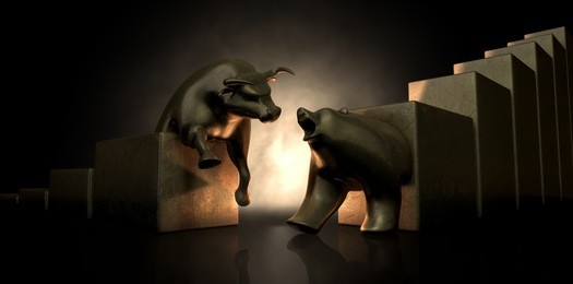 an abstract closeup of two gold cast statuettes depicting a stylized bull and a bear in dramatic contrasting light representing a financial market trends on an isolated dark background