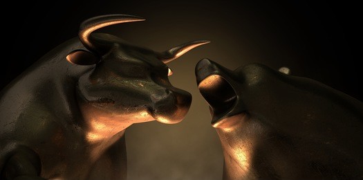 an abstract closeup of two gold cast statuettes depicting a stylized bull and a bear in dramatic contrasting light representing a financial market trends on an isolated dark background