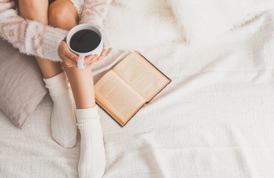 soft photo of woman on the bed with old book and cup of coffee in hands, top view point. cozy, comfy, soft