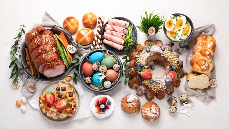 traditional easter dinner or  brunch with ham, colored eggs, hot cross buns, cake and vegetables. easter meal dishes with holday decorations. top view, flat lay