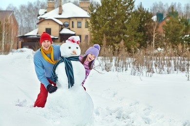 funny dad and daughter with a snowman. family walking outdoors in winter
