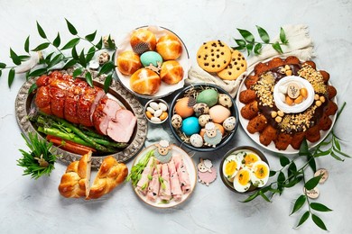 classic easter ham dinner. top view table scene on a white background. ham, eggs, hot cross buns, carrot, cake and vegetables.