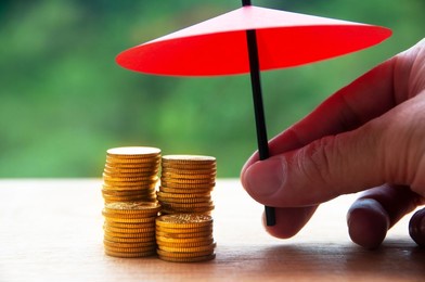 umbrella covering gold coin with blurred nature background. security, financial independence, assurance and safety concept.