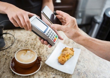 cropped image of customer paying through mobilephone over electronic reader at cafe counter