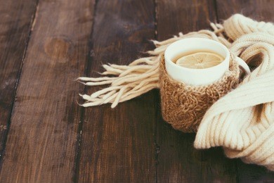 cup of hot tea with lemon dressed in knitted warm winter scarf on brown wooden tabletop, soft focus