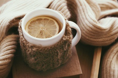 cup of hot tea with lemon dressed in knitted warm winter scarf on brown wooden tabletop, soft focus