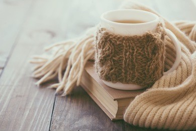 cup of hot tea with lemon dressed in knitted warm winter scarf on brown wooden tabletop, soft focus