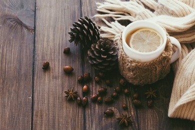 cup of hot tea with lemon dressed in knitted warm winter scarf on brown wooden tabletop, top view point