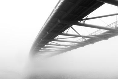 black and white photo of a steel bridge over a river in fog, cracow, poland