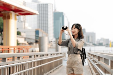 young asian woman backpack traveler using a camera in express boat pier on chao phraya river in bangkok. journey trip lifestyle, world travel explorer or asia summer tourism concept. 