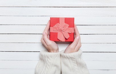 female hands holding gift on wooden table.