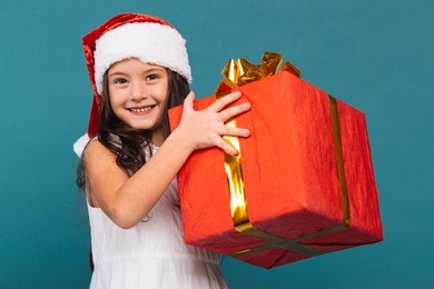 smiling funny child (kid, girl) in santa red hat holding christmas gift in hand. christmas concept.