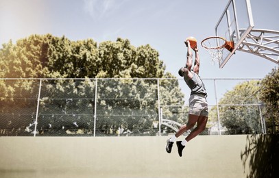 full length of basketball player dunking a ball into the net during a match on a court. fit and active athlete jumping to score during a competitive game. healthy athletic african man in action