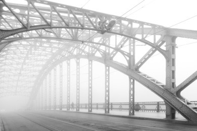 black and white photo of a steel bridge over a river in fog, cracow, poland