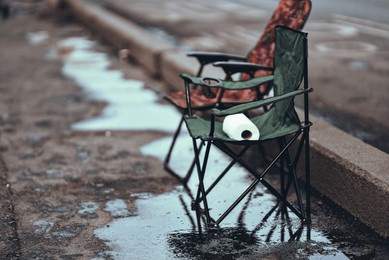 the photo shows a folding chair with a roll of toilet paper on top, placed in the middle of a pedestrian bridge over calm waters. its purpose and significance are unclear.